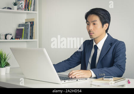 Portrait Asian Businessman in Formal Navy Blue Suit Using Laptop and Working in Office. Asian businessman with laptop and smartphone Stock Photo
