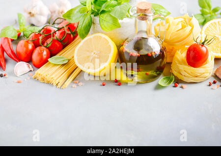Italian food ingredients – pasta, tomatoes, basil and olive oil on gray concrete background. Stock Photo