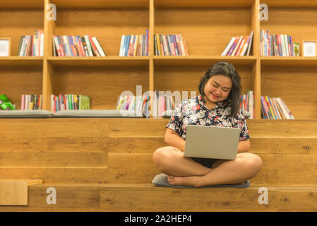 Young student girl using laptop near well decorated library bookshelf  Stock Photo