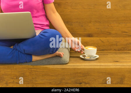 Calm woman using laptop and having cappuccino with wooden background Stock Photo