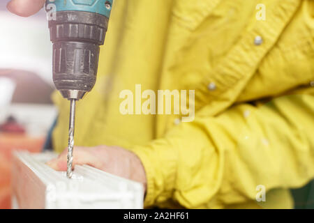 A male worker prepares a plastic (UPVS) window for installation, drilling a hole with a battery screwdriver. Close-up. Stock Photo