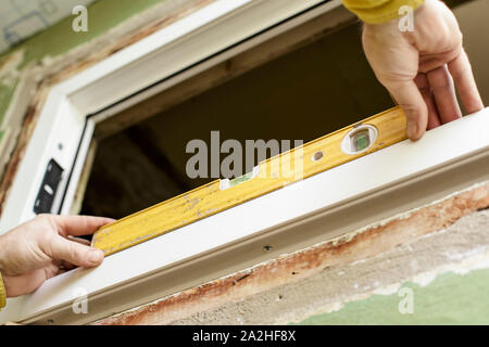 The male worker installs (UPVS) a window inside the premises using a level. Stock Photo