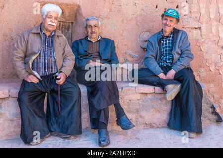 Three Iranian men sitting on a brick bench, Abyaneh village, Esfahan Province, Iran Stock Photo