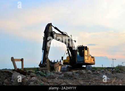 Heavy tracked excavator at a construction site on a background of a residential building and construction cranes on a sunny day against the backdrop o