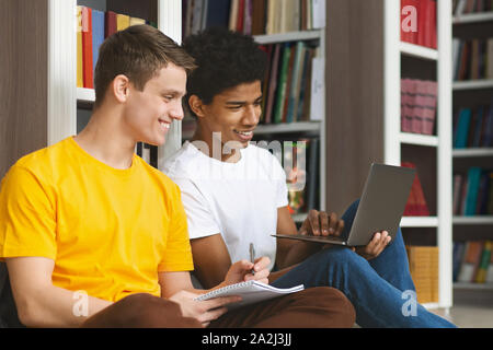 Two young guys sitting on floor in campus library Stock Photo