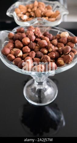 Hazelnuts and and almonds in a glass bowls on a black background with a reflection Stock Photo