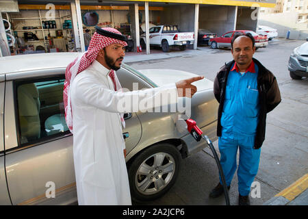Saudia Arabia Saoedi Arabie Riyad Riaad Petrol for the car. A workingmigrant is helping a local Saudi man in traditional dress called a thobe or thawb Stock Photo