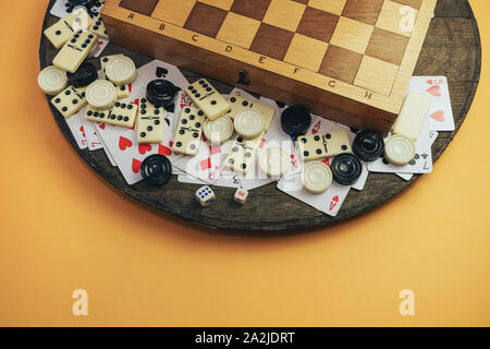 Various board games chess board, playing cards, dominoes on a old wooden table orange background. Stock Photo