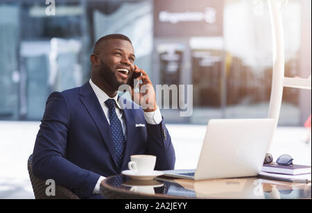 Happy Entrepreneur Speaking On Phone Working In Outdoor Cafe Stock Photo