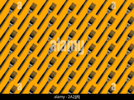 Many black plastic forks on yellow background, top view. Disposable table wear concept. Creative top view pattern. Stock Photo
