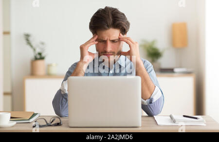 Millennial Guy Suffering From Headache Working On Laptop Indoor Stock Photo