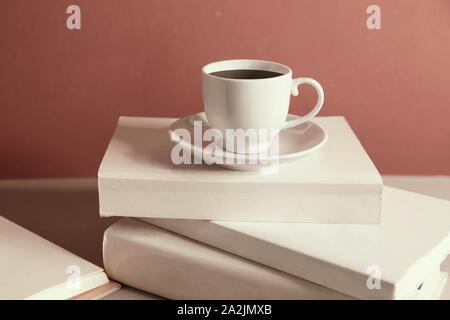 Cup of coffee over the stack of closed books, red wall background Stock Photo