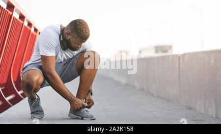 Afro guy checking on his shoelaces on bridge Stock Photo