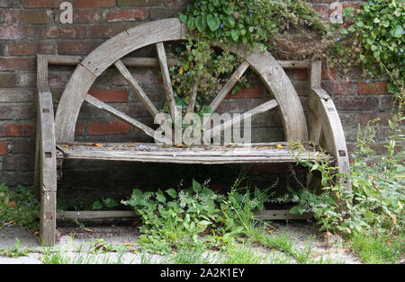 Handcrafted wooden bench with ivy and brick wall Stock Photo