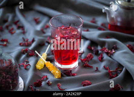 Refreshing red hibiscus tea with ice and rock candy sticks on a grey cloth Stock Photo