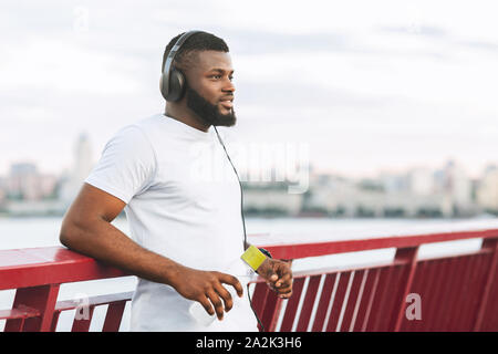 Dreamy black athletic guy resting on city bridge Stock Photo