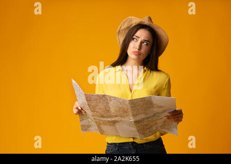 Pensive Tourist Girl Holding Map Planning Vacation On Yellow Background Stock Photo