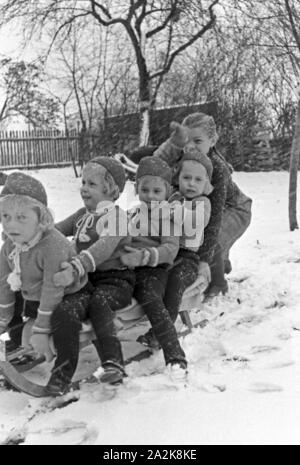 Schlittenfahren an Weihnachten bei einer Familie mit Vierlingen, Deutschland 1930er Jahre. Riding a sleigh at christmas at a family with quadruplet girls, Germany 1930s. Stock Photo