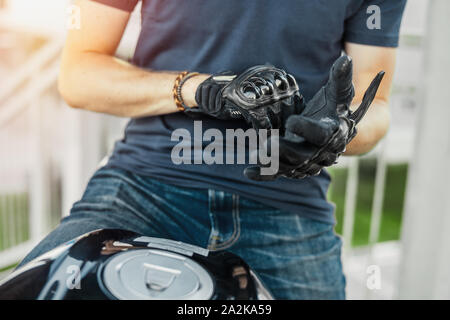 Close up of biker putting on black gloves and sitting on motorcycle. Front view. Stock Photo