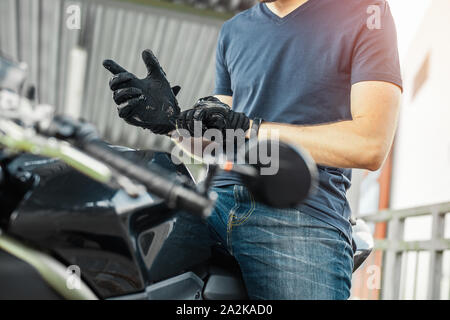 Close up of biker putting on black gloves and sitting on motorcycle. Side view. Stock Photo