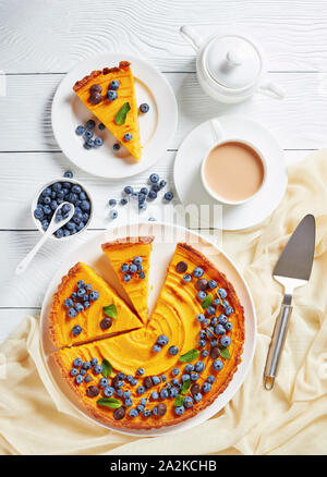 sliced pumpkin pie decorated with blueberries, orange zest and fresh mint on white plate on a white wooden table served with hot cocoa, view from abov Stock Photo