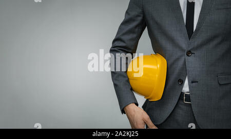 construction industry business - businessman holding yellow hard hat underarm on gray background with copy space Stock Photo