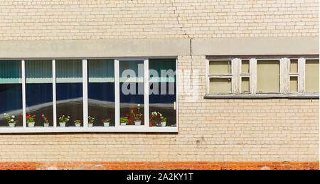 The wall of the old brick building, with a window with wooden frames, on the windowsill is blooming geranium. Stock Photo