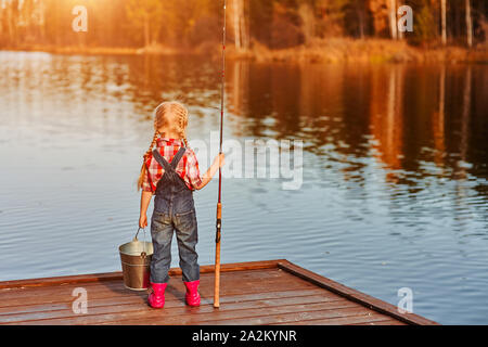 A little girl with a fishing rod looks at the catch of fish in a