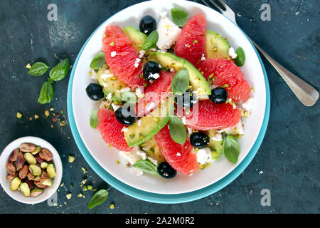 Avocado salad with grapefruits, feta cheese, black olives and pistachio. Top view with copy space. Healthy food. Stock Photo