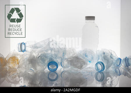 a empty plastic bottle standing among many crushed plastic bottles and a reclycle symbol on the white background Stock Photo