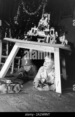 Two boys playing soldiers with a steel helmet and a toy rifle under the christmas tree, Germany 1930s Stock Photo