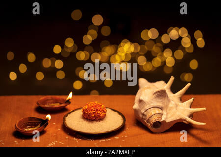 Diwali festive decoration with diya oil lamps, flowers, rice grains and hindu religious conch shell shankha isolated in bokeh lights black background. Stock Photo