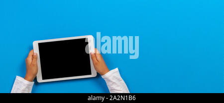 Kid hand holding white tablet computer on light blue background Stock Photo