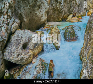Whirling light blue mountain stream rushing over the cascades between the rounded rocks Stock Photo