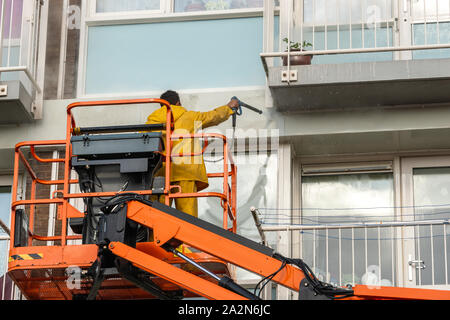 person in rain suit standing on an orange platform is spraying the concrete of a flat with a high pressure cleaner Stock Photo