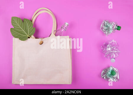 Reusable cotton bag with a glass bottle and a sheet of figs and three crumpled plastic bottles on a bright pink fuchsia background. Zero waste concept Stock Photo