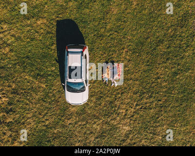 overhead aerial view car at green grass field couple laying on blanket Stock Photo
