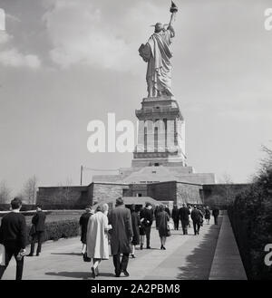 1960s, historical, visitors walking up a path towards the Statue of Liberty, a colossal neoclassical sculpture on Liberty Island in New York Harbour in New York City, USA. The copper statue was a gift from the people of France. Designed by French sculptor Frédéric Auguste Bartholdi, its metal structure was built by Gustave Eiffel, he of the famous tower in Paris. Stock Photo