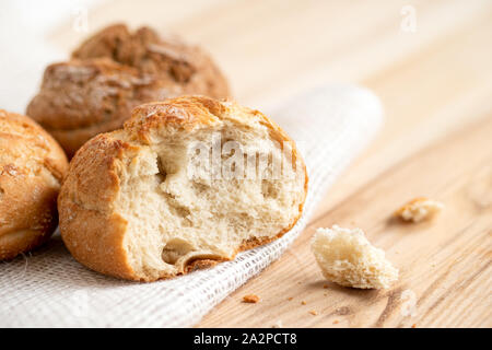 Broken round rustic white bread roll next to two round bread rolls on white burlap on light wood. Stock Photo