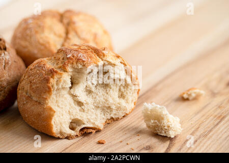 Broken round rustic white bread roll next to two round bread rolls on light wood. Stock Photo