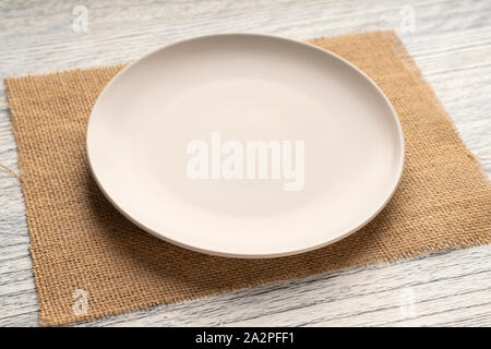 Beige round plate on a sackcloth on a wooden white table. Copyspace for labels and menus Stock Photo