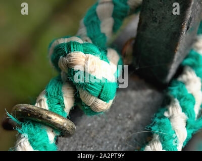 A thick rope in green and white striped, close-up of a knot, the rope is led through a metal ring. Stock Photo