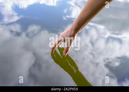 womans had touching the surface of a lake, reflections of hand and sky Stock Photo
