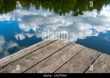wooden jetty at the edge of a lake with reflections of the sky Stock Photo