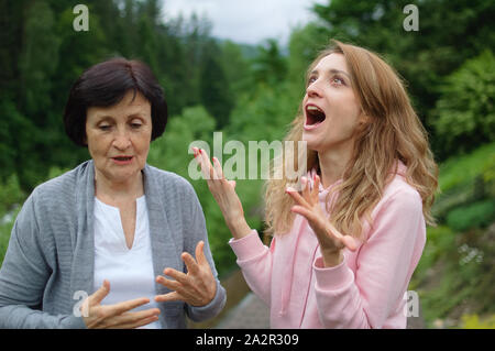 Outdoors portrait of senior mother and adult daughter are communicating outside over landscape of forest and mountains. Two generations, problems Stock Photo