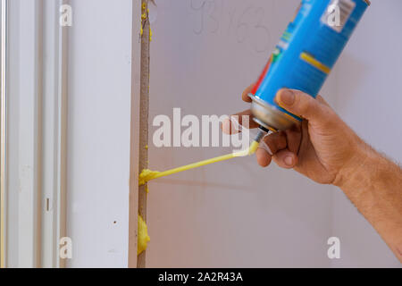 Man using polyurethane foam for installing a window on a handsome worker in action during the installation Stock Photo