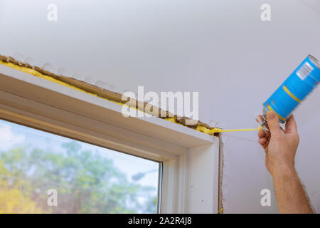 Man in a using a mounting foam the window and the wall with insulation foam to insulate Stock Photo