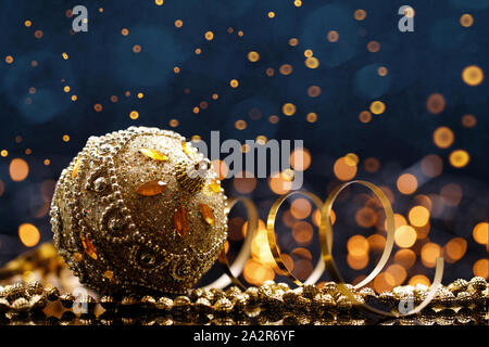 Festive Christmas gold ball with decoration on dark blue background with sparks.