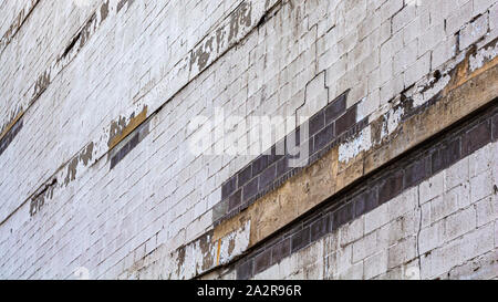 Paint is cracked, peeling and falling off an otherwise white brick wall, showing a building that has not been maintained. Stock Photo