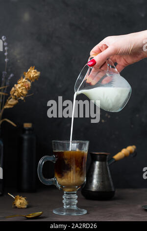 Woman's hand pouring milk in to coffee, hot drink, trendy dark style image. Frozen motion. Stock Photo